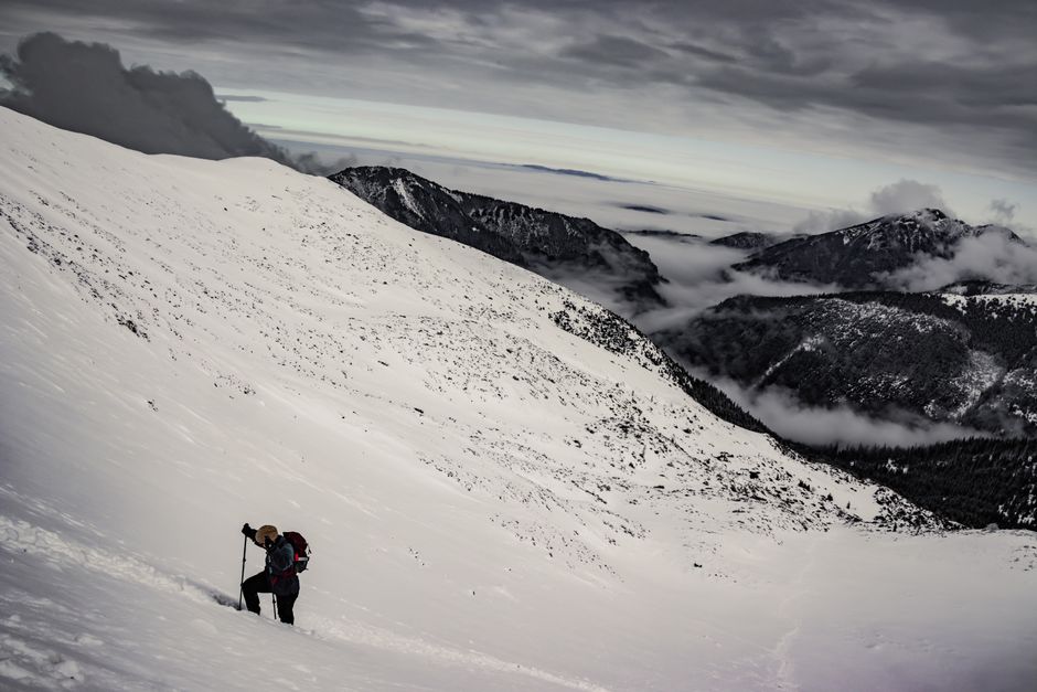 Daring hiker scaling a snowy mountain in winter, with dramatic clouds and rugged terrain.