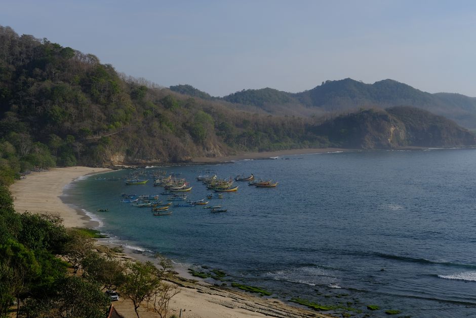 A tranquil coastal scene with fishing boats and lush hills under a clear sky.