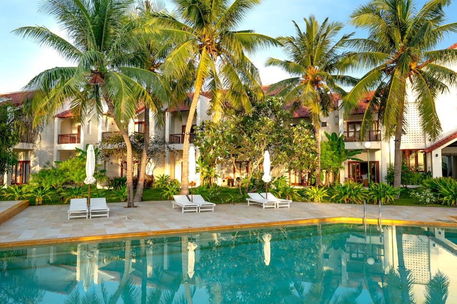 Serene resort featuring a swimming pool surrounded by palm trees and villas.