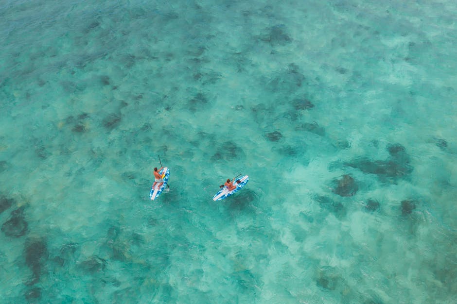 Aerial shot of two people paddleboarding in crystal-clear turquoise water, perfect for summer vacation.