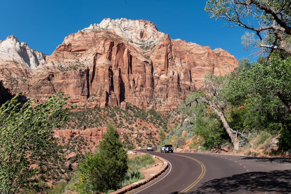 Captivating view of Zion National Park's towering red cliffs along a winding road under a clear blue sky.