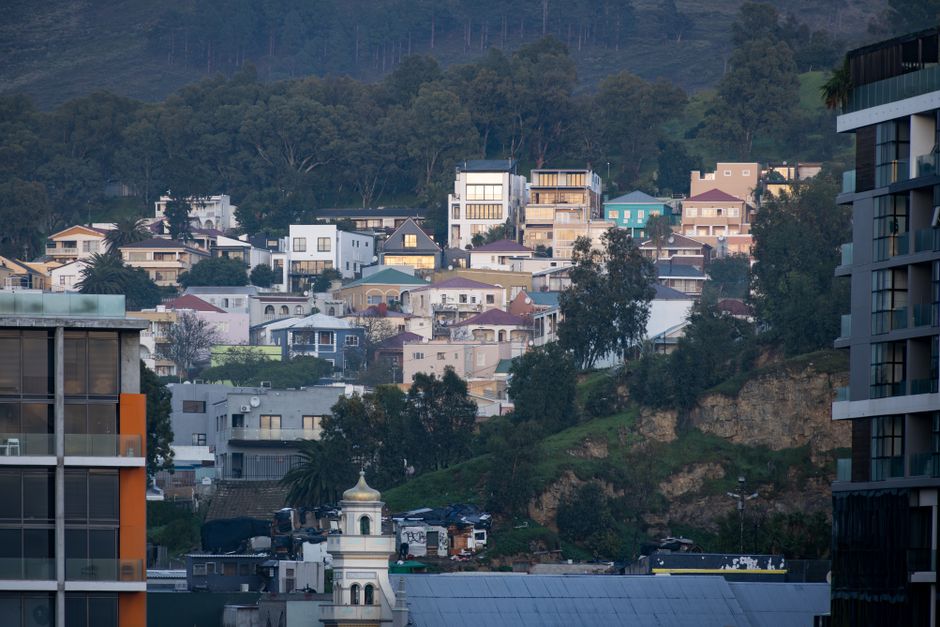 A serene view of a hillside urban neighbourhood with diverse houses nestled among trees during the day.