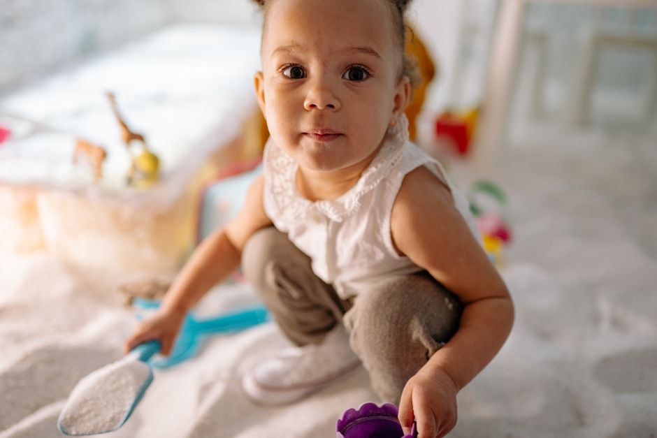Cute toddler engaging in play with toys in an indoor sandbox setting, embracing childhood joy.
