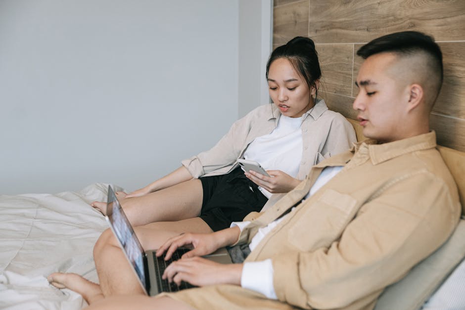 A couple using devices on a bed, enjoying technology in a relaxed indoor setting.