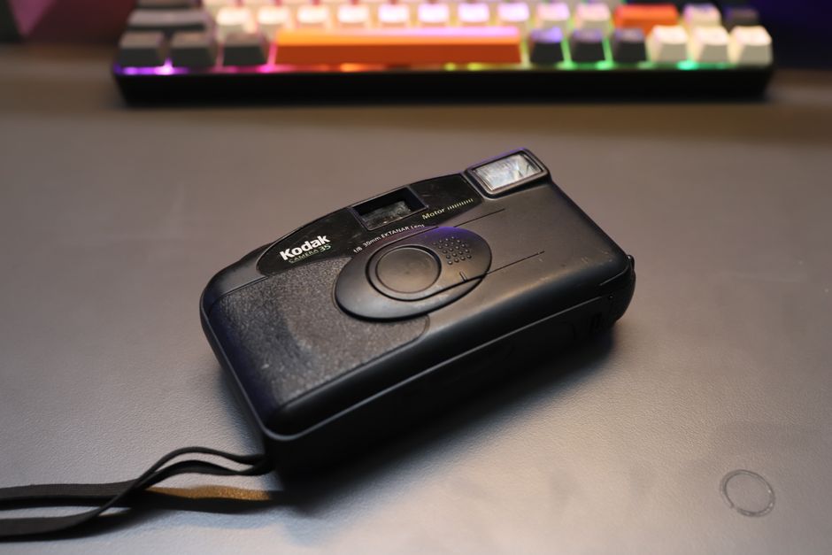 Close-up of a vintage Kodak camera on a modern desk with a colorful mechanical keyboard in the background.