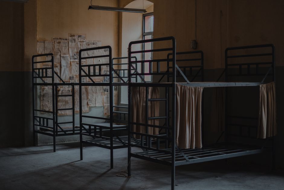 Old fashioned metal bunk beds with blinds placed in row at wall in spacious room of neglected house with window