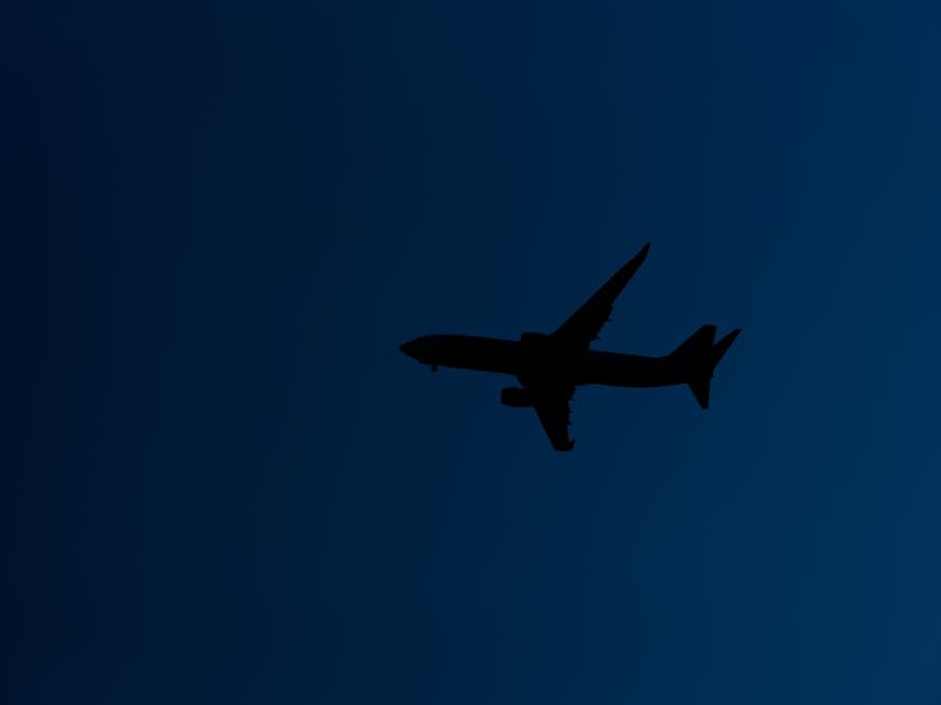 Silhouette of an airplane flying against a blue evening sky, showcasing graceful flight.