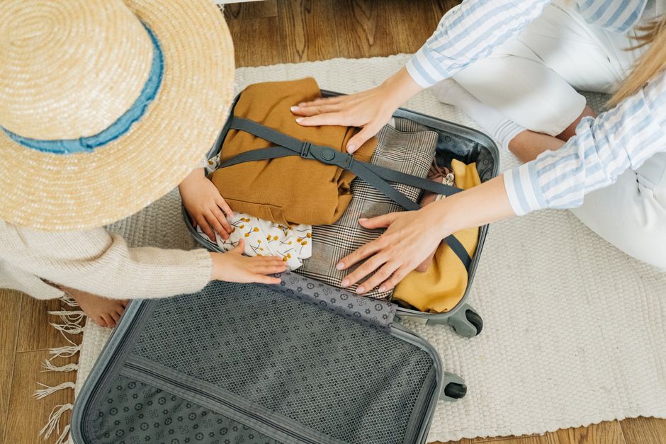 A woman and child pack clothes in a suitcase, preparing for a holiday.