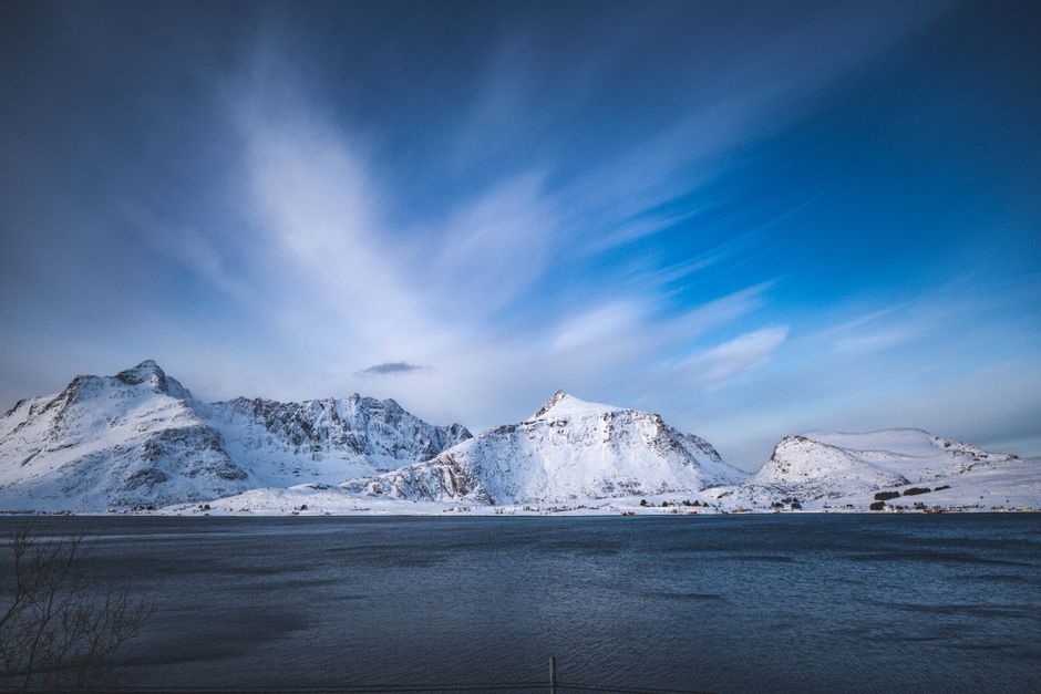 Scenic view of snow-covered mountains and ocean in Lofoten under a clear sky.