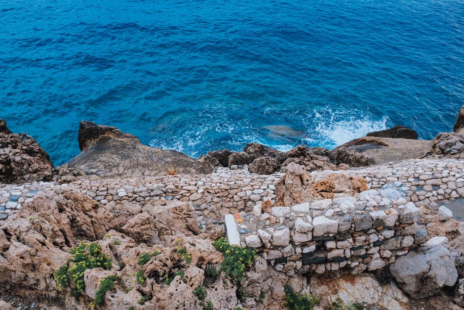 Beautiful rugged coastal path alongside deep blue ocean waves crashing on rocks.