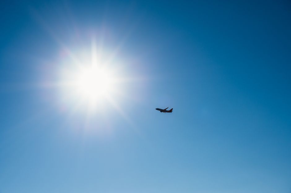 Airplane flying under a radiant sun in a clear blue sky, capturing a sense of freedom and travel.