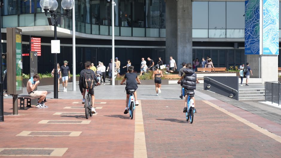 People biking and walking in a modern urban plaza with contemporary architecture.