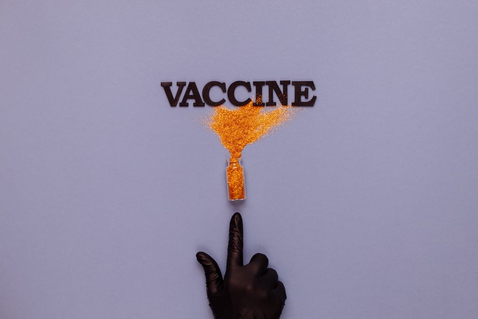 Creative depiction of vaccine using orange glitter, black glove, and text.