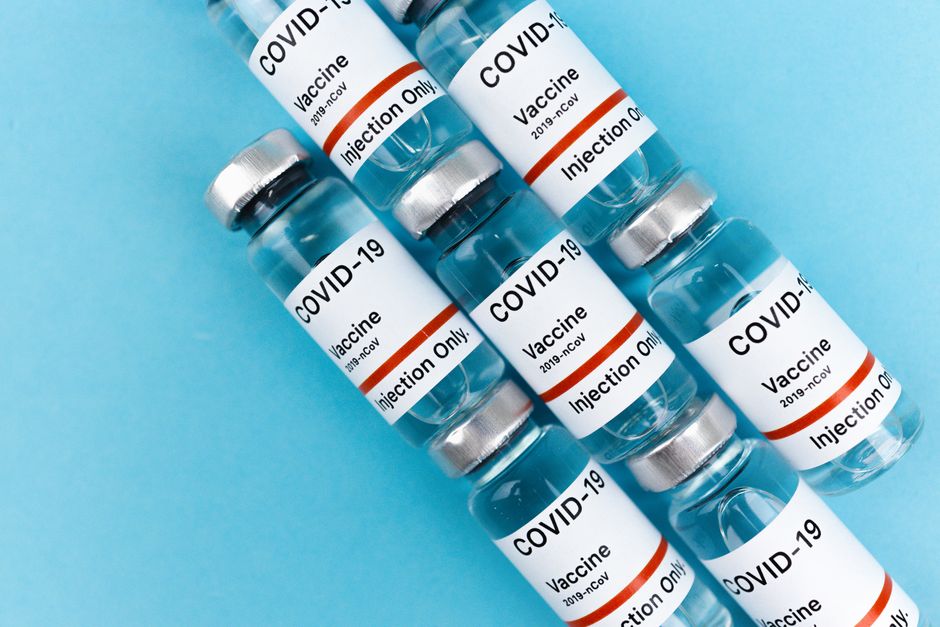 Array of COVID-19 vaccine vials labeled for injection lying on a blue background.