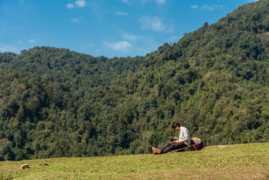 A man relaxes while reading a book on a hillside in Pokhara, Nepal. Embracing nature's tranquility.